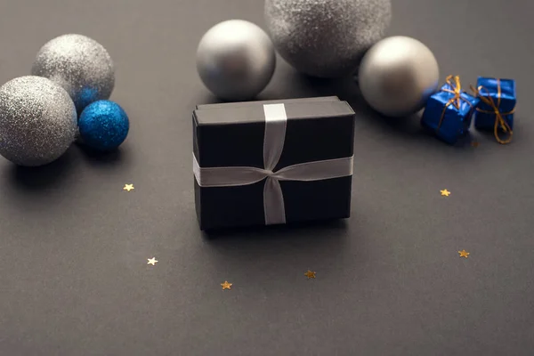 Küçük bir hediye kutusu ve yıldızlı karanlık bir arka planda Noel topları.