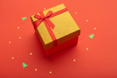 Kırmızı ve altın renkli hediye kutusu, parlak kırmızı bir zemin üzerinde altın yıldızlar ve küçük Noel ağaçları..