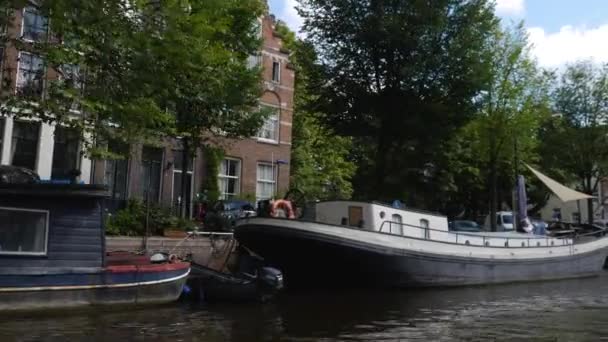 夏日阳光明媚的时候 在阿姆斯特丹的房屋和建筑物旁边 沿着运河坐着一艘小船 — 图库视频影像