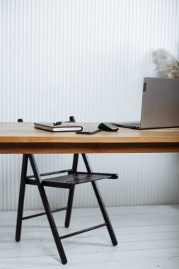 Masanın üzerinde bir sandalye, bir dizüstü bilgisayar, bir düzenleyici, bir kalem ve bir bilgisayar faresi var.