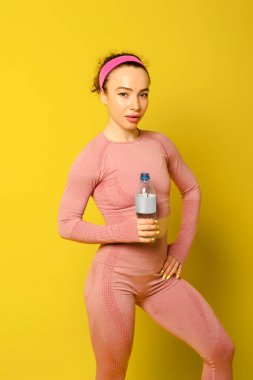 Hoş fitness kızı elinde şişeyle kameraya bakıyor, boş zaman, boş zaman, yaşam tarzı. İzole edilmiş sarı arka plan. Stüdyo. kopyalama alanı. Boş zaman