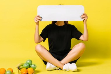 Siyahlı kız bacak bacak üstüne atmış ve sarı stüdyo arka planında boş reklam panosu tutuyor.