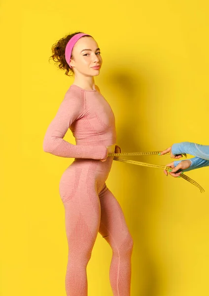 Spor giyimli güzel, ince bir kadın göbeğini ya da belini bir bantla ölçüyor. Diyet ve spor konsepti