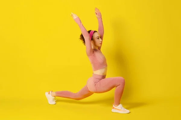 Antrenman yapıyorum. Pembe dar spor kıyafetleri içindeki genç kıvırcık kadın egzersiz yapıyor. Kopyala Space.Stüdyo resmi sarı arka planda izole edildi.