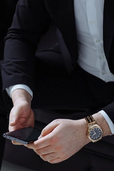 Takım elbiseli bir iş adamı deri koltuğa oturur ve elinde bir akıllı telefon tutar.
