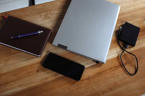 Ahşap masadaki akıllı telefon akıllı telefon, günlük, dizüstü bilgisayar, sabit disk ve kalem.