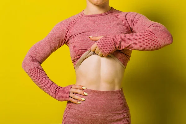 Şişirilmiş karın kaslarının görüntüsü. Pembe spor elbiseli sporcu kadın..