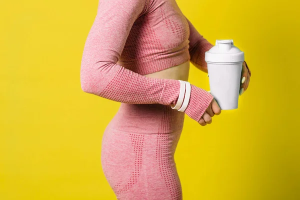 Beyaz protein içeceği ya da bir şişe su taşıyan pembe spor giysili atletik bir kadın.