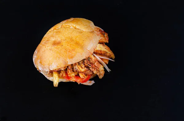 Chicken doner kebab on hamburger bun. Doner kebab in bread on wooden board on black background.