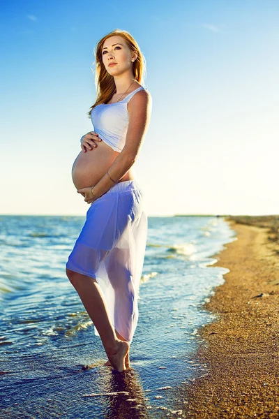 Piękna kobieta w ciąży z Rude włosy, spacery na plaży niebieski — Zdjęcie stockowe