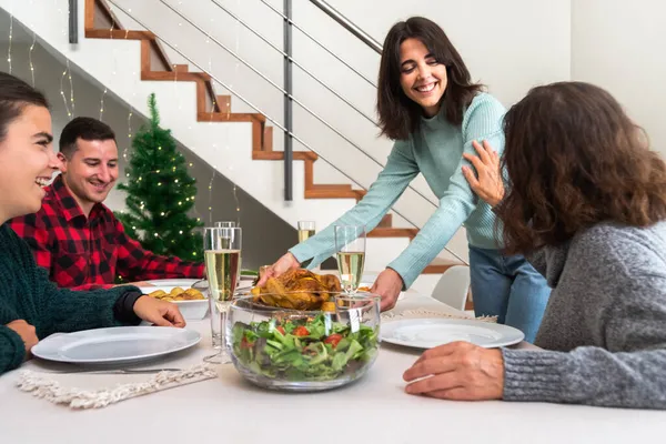 Usmívající se mladá běloška přináší pečené kuře na stůl. Vánoční rodinná sešlost. — Stock fotografie