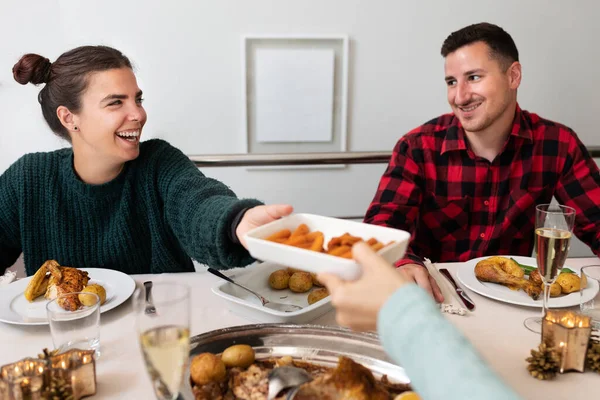 Usmívající se mladý bělošský pár na vánoční rodinné večeři. Podávám nějaké předkrmy.. — Stock fotografie