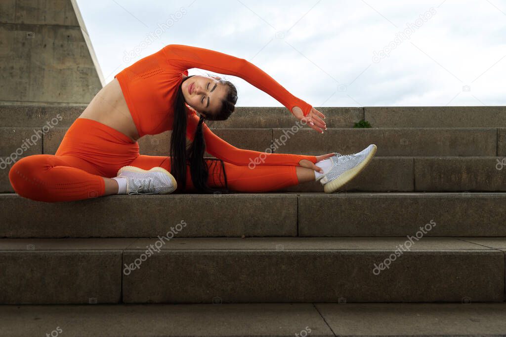 Young brunette female runner stretching side body before jogging. Woman athlete morning workout routine.