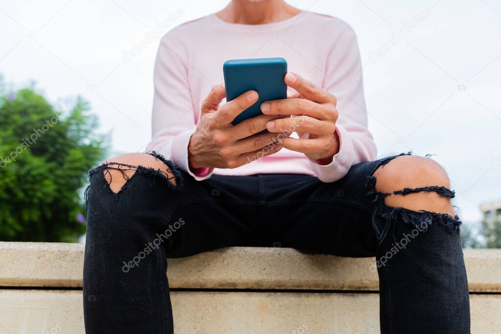 Unrecognisable caucasian man with pink sweater holding cellphone reading text messages. Using mobile phone apps.
