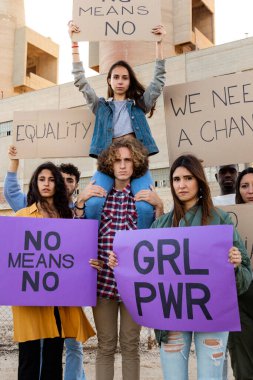 Young female protester sitting on mans shoulders holds a no means no signs in a demonstration. Vertical image.