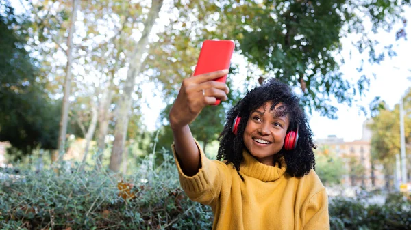 Panoramic image of young African American woman taking a selfie with smartphone in a park. Copy space. — Stockfoto