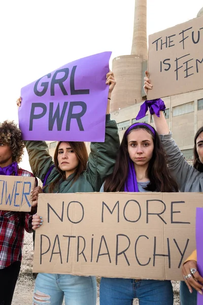 Young woman looking at camera holding No more patriarchy banner in feminist demonstration for womans rights. Vertical.