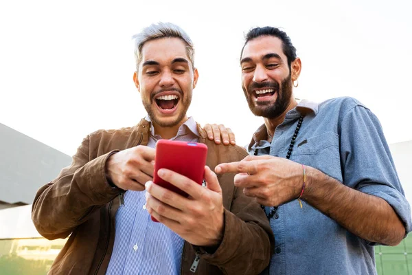 Unga manliga homosexuella par tittar på mobilen. Kaukasiska män titta på roliga videor på mobiltelefon tillsammans. — Stockfoto