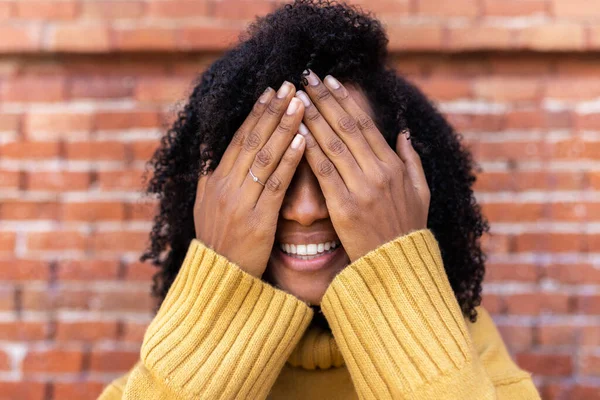 Smiling African American woman with curly hair covering her eyes with hands. — Stockfoto
