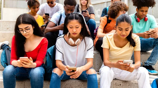 Grupo de estudantes multirraciais do ensino médio usando telefone celular ignorando uns aos outros. Viciado em mídias sociais. — Fotografia de Stock