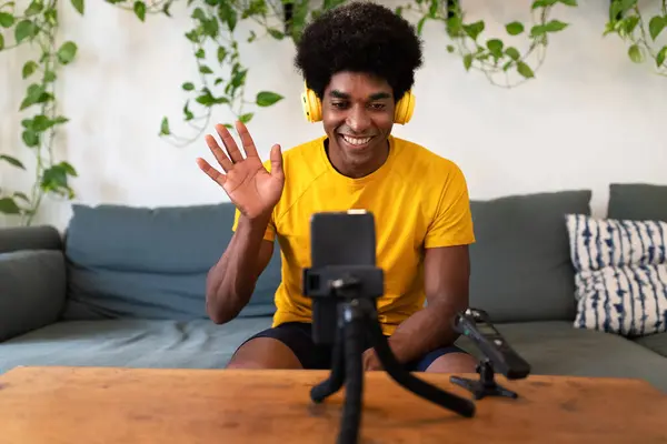 Ung afrikansk amerikansk influencer vinkar hej till anhängare. Spela in sig själv för video tutorial med mobiltelefon. — Stockfoto