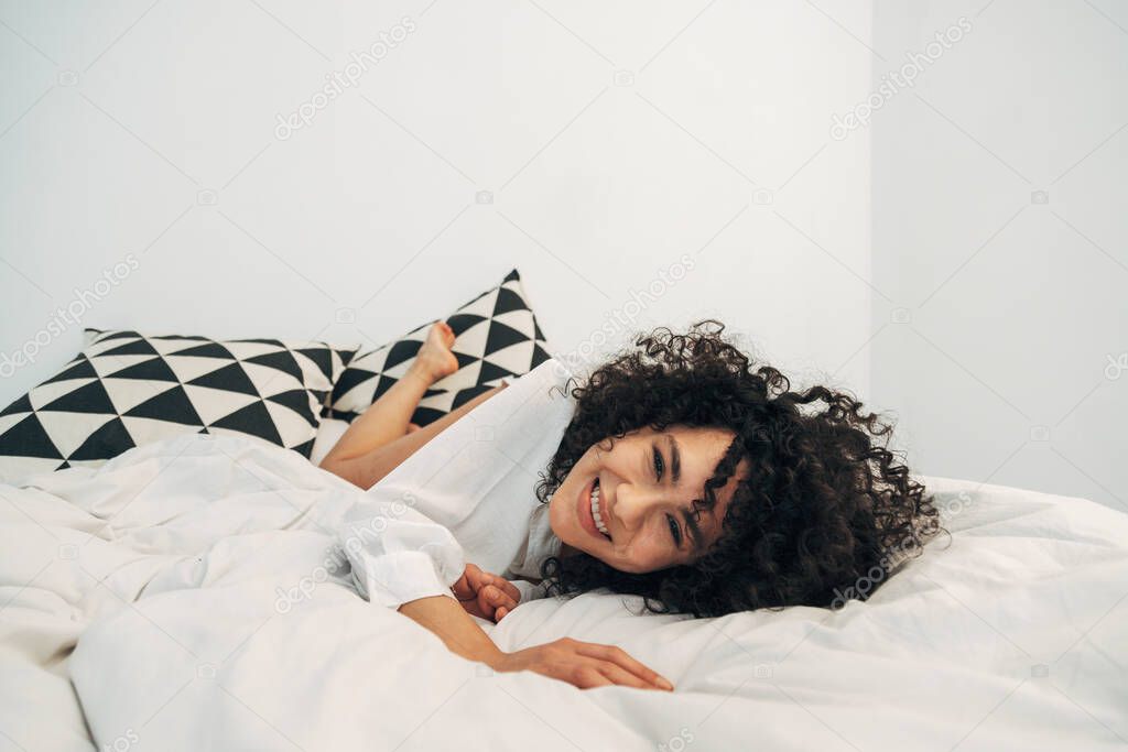 Smiling playful mixed race woman lying on bed looking at camera. Copy space.