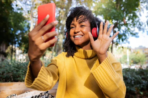 Sonriente joven afroamericana ola mano en videollamada utilizando el teléfono móvil al aire libre. —  Fotos de Stock