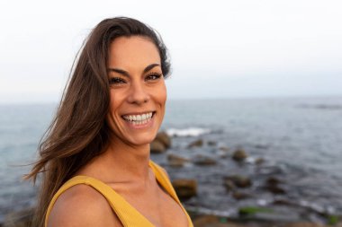 Okyanusun yakınındaki kameraya bakan gülümseyen beyaz kadın portresi. Boşluğu kopyala.