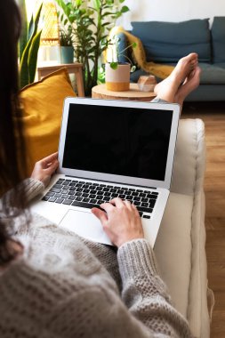 Kafkasyalı genç bir kadın dizüstü bilgisayar kullanıyor ve evinde kanepede uzanıyor. Dikey resim