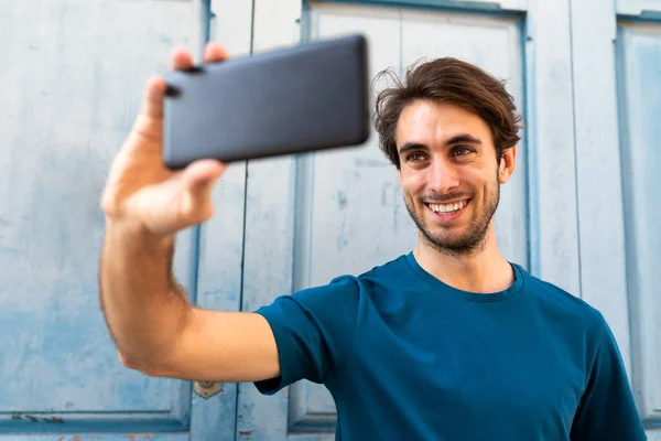 Ung kaukasisk man tar en selfie med smartphone utomhus. Selektivt fokus på ansiktet. — Stockfoto