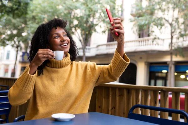 Ung afroamerikansk kvinna som tar selfie med hjälp av smartphone samtidigt som kaffe i utomhus café terrass. Kopiera utrymme. — Stockfoto