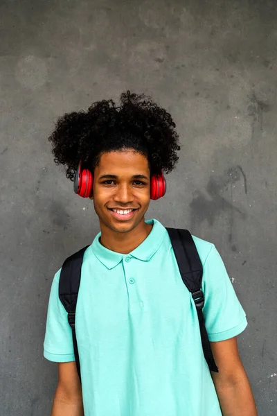 Retrato vertical de adolescente feliz chico afroamericano con peinado afro mirando a la cámara con auriculares. —  Fotos de Stock