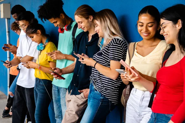 Gelukkige en lachende groep multiraciale middelbare scholieren die mobiele telefoon gebruiken die tegen de blauwe muur staat. Sociale media. — Stockfoto
