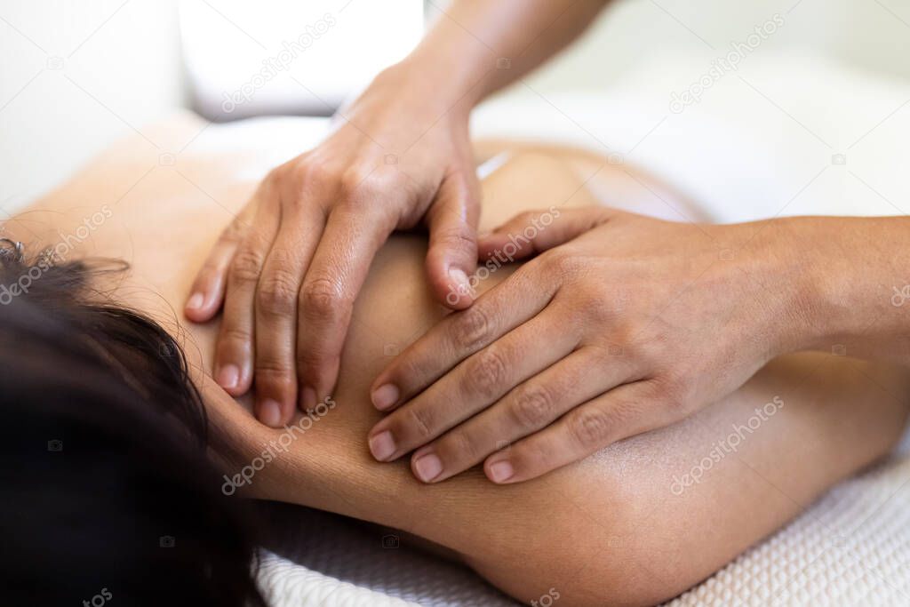 Closeup of woman hands giving a relaxing back massage to female client.