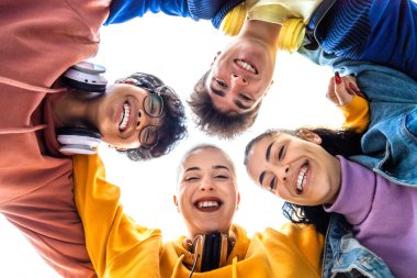 Düşük açılı bir bakış açısı olan genç kolej öğrencisinin kafaları çember içinde kucaklaşması. Lise arkadaşları gülümsüyor daire şeklinde sarılıyorlar..