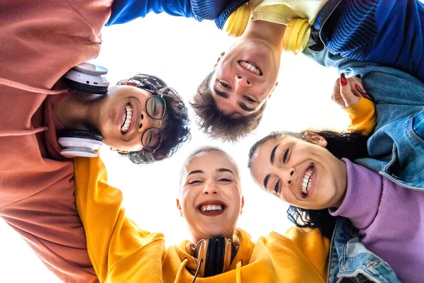 Düşük açılı bir bakış açısı olan genç kolej öğrencisinin kafaları çember içinde kucaklaşması. Lise arkadaşları gülümsüyor daire şeklinde sarılıyorlar..