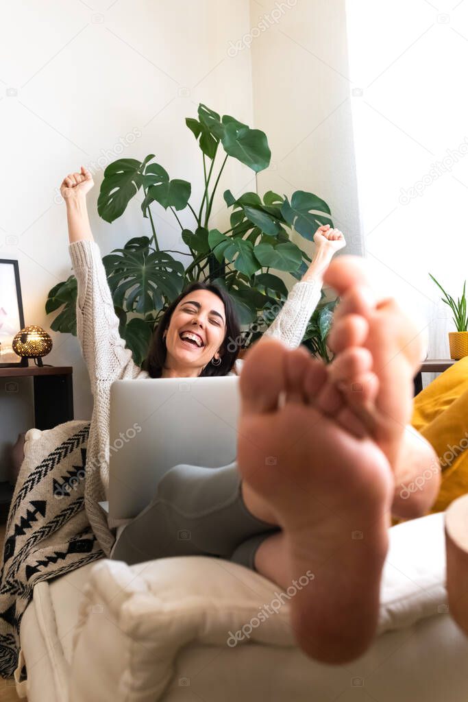 Excited young caucasian woman raising arms up celebrating success at home using laptop. Copy space. Vertical.