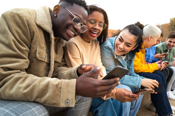 Gelukkig multiraciale tiener college studenten hebben plezier met behulp van mobiele telefoon samen in de campus buiten. — Stockfoto