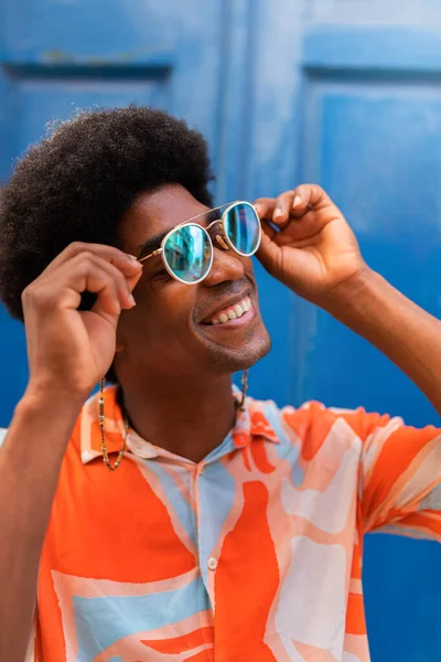 Vertical portrait of young happy black man putting on sunglasses outdoors. — Stockfoto