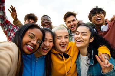 Bir grup çok ırklı üniversite arkadaşı dışarıda eğleniyor. Mutlu insanlar selfie çekiyor..