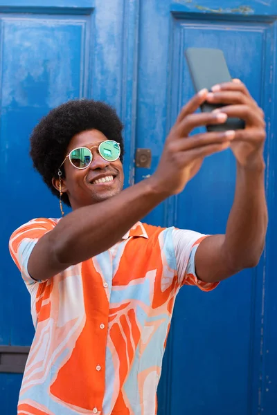 Giovane felice uomo nero prendendo selfie con il telefono cellulare all'aperto. Immagine verticale. — Foto Stock