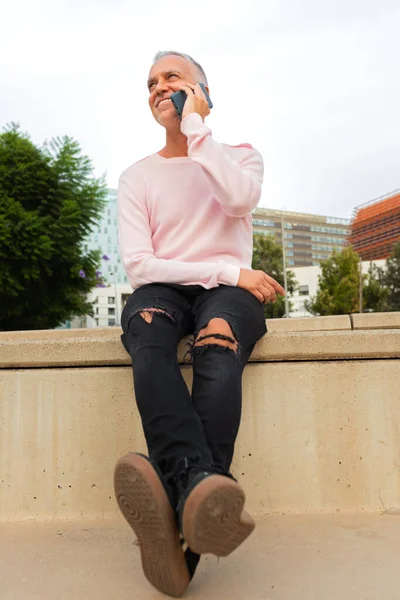 Smiling caucasian man talking on mobile phone sitting on stairs in the city. Vertical image. Lifestyle.