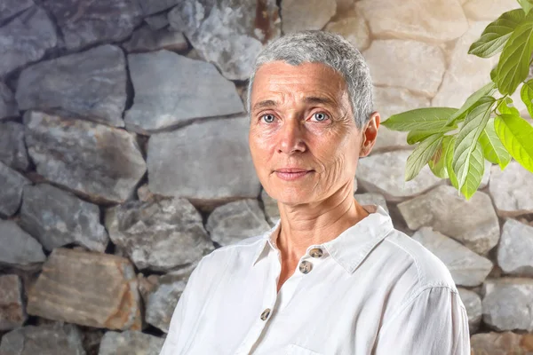 Taş çitin yanındaki mutlu yaşlı kadının portresi.