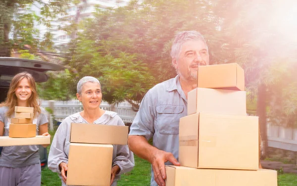 A happy family moves the boxes from the car to their new home. Moving with cardboard boxes