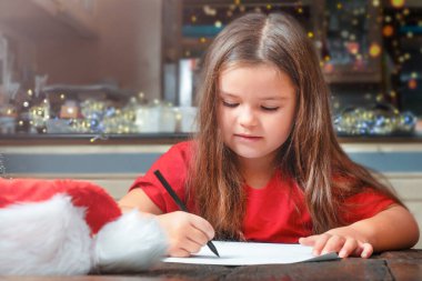 Çocuk kız Noel Baba 'ya mektup yazıyor.