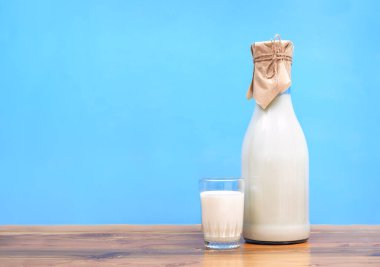 Bardaktaki süt ve mavi arka plandaki ahşap masanın üzerindeki cam şişe.