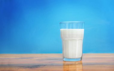 Glass of milk on wooden surface against blue background
