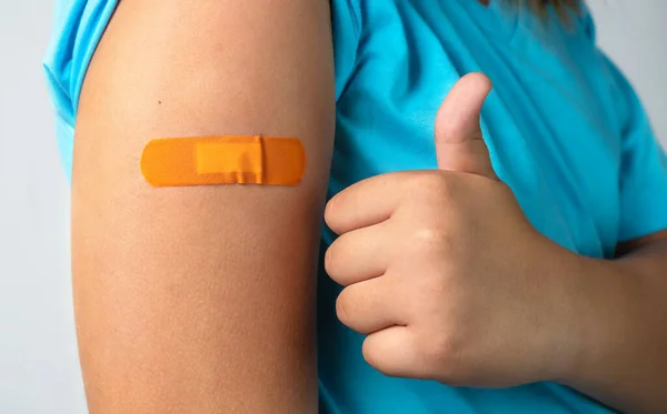 Child shows thumbs up near vaccination patch