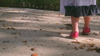 Çocuk parkta yürüyor ve ağaç yapraklarını tekmeliyor.