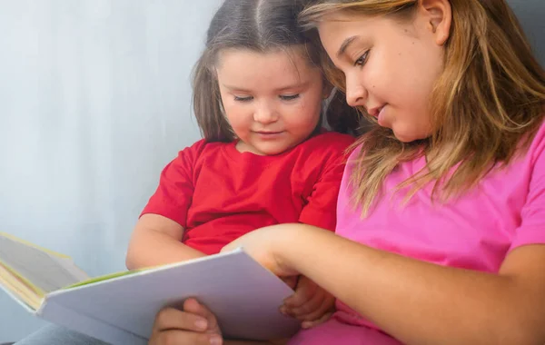 Старшая Сестра Помогает Ребенку Читать Книгу Диване — стоковое фото